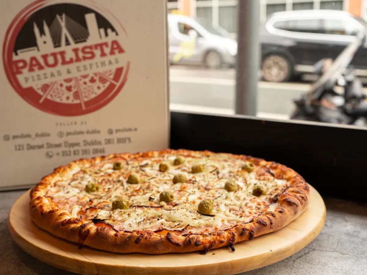 A Paulista pizza on a wooden board beside the branded delivery box